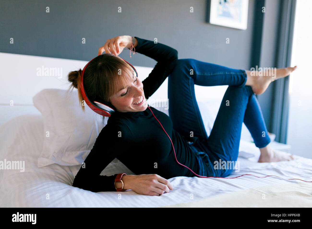 Happy young woman lying on bed wearing headphones Stock Photo - Alamy