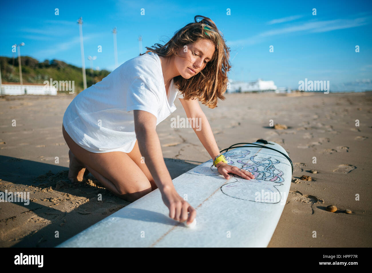 Young woman applying paraffin on  surfboard on the beach Stock Photo