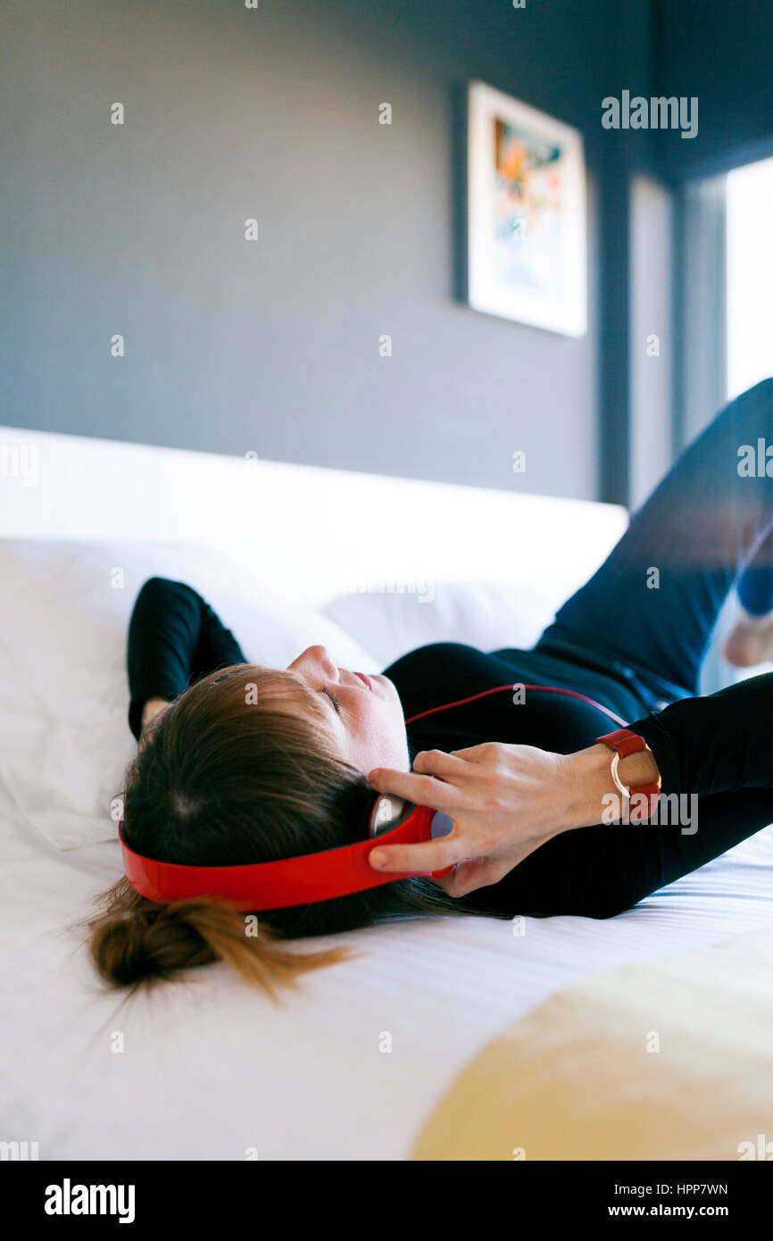 Relaxed young woman lying on bed wearing headphones Stock Photo - Alamy