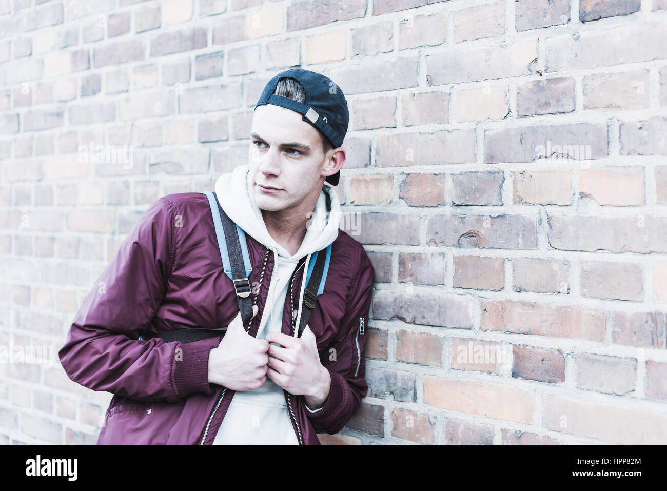 Portrait of young man leaning against brick wall Stock Photo - Alamy