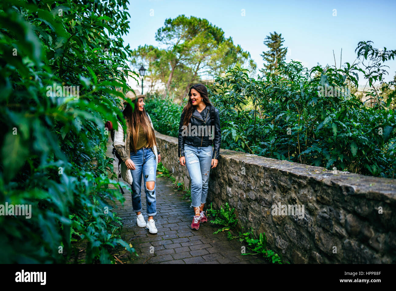 Two smiling young women walking on a path with plants Stock Photo - Alamy