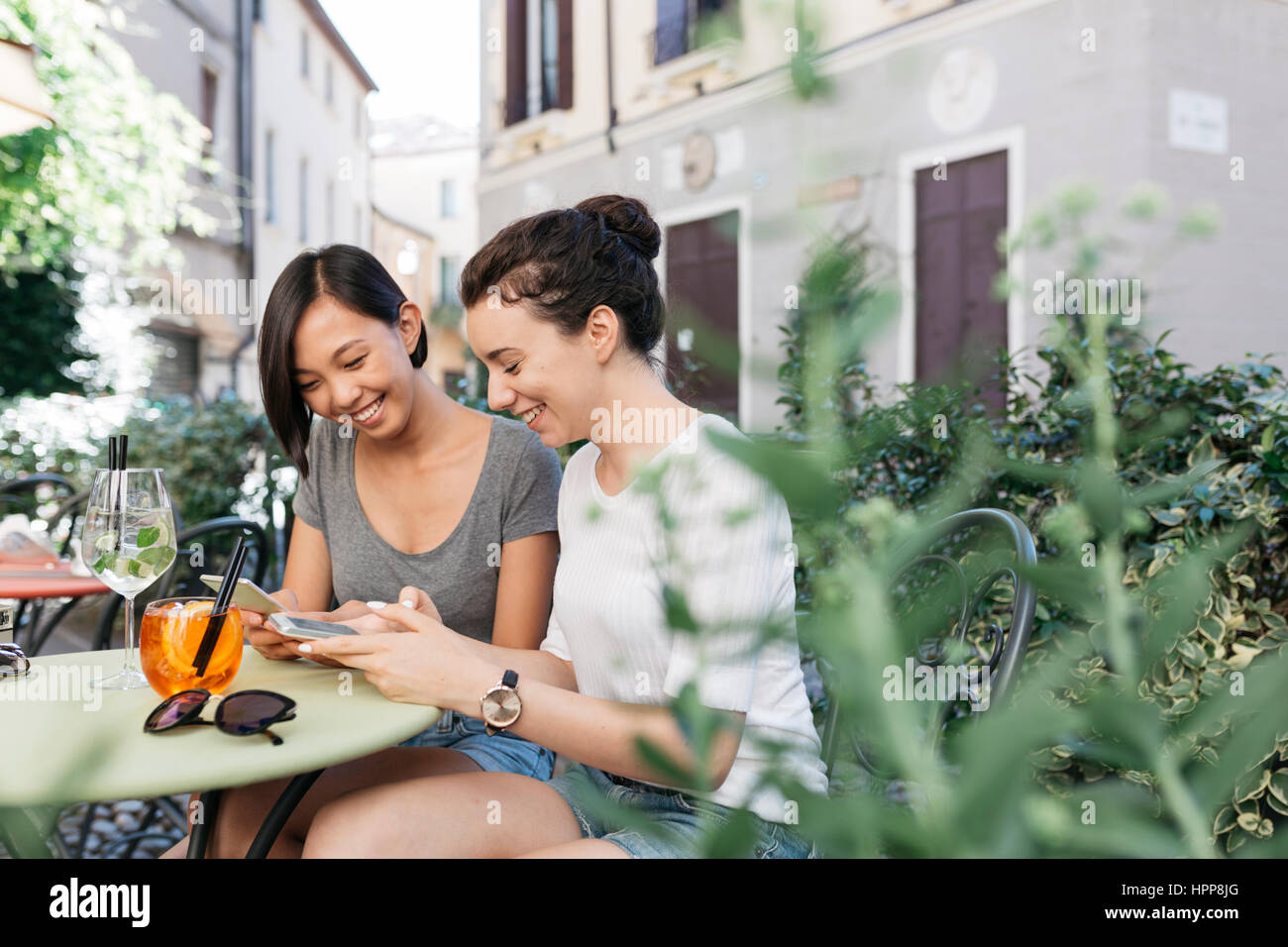 Italy, Padua, two young women checking their cell phones at sidewalk cafe Stock Photo