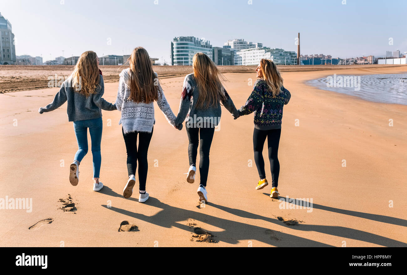 Spain, Gijon, back view of four friends running hand in hand on ...