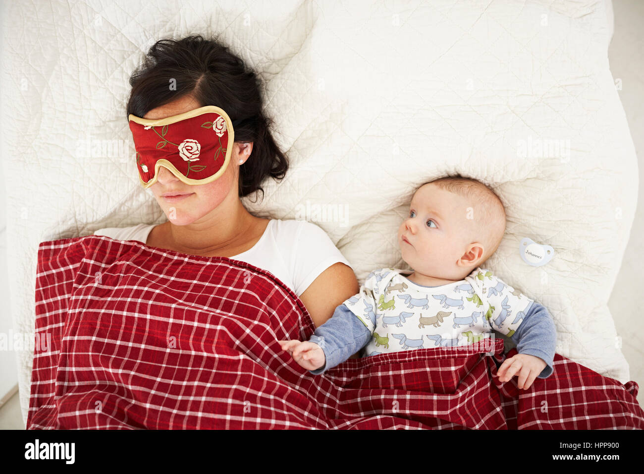 Mother with sleep mask and awake baby lying in bed Stock Photo Alamy