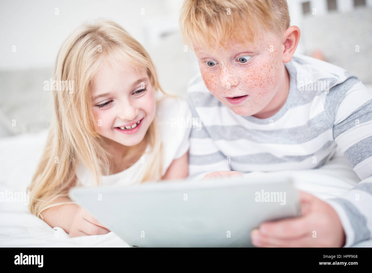 Brother and sister lying in bed using tablet Stock Photo - Alamy