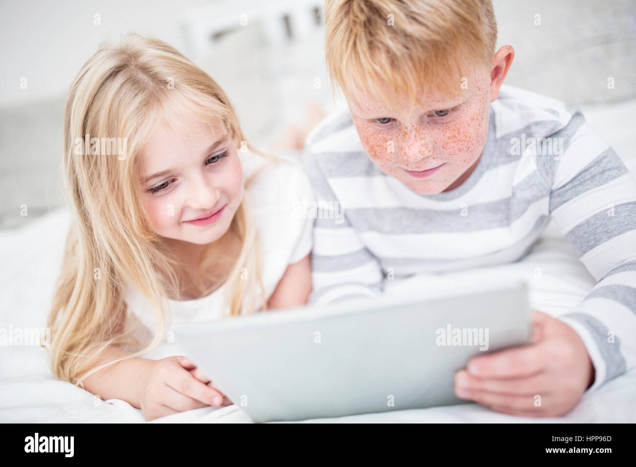 Brother and sister lying in bed using tablet Stock Photo - Alamy