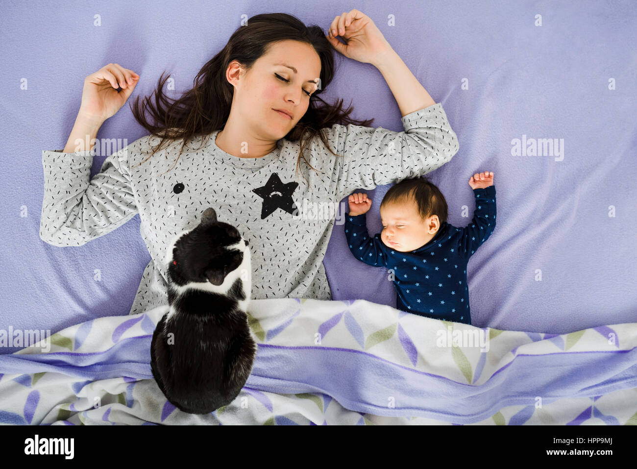 Newborn baby girl and mother sleeping in bed with cat watching Stock Photo