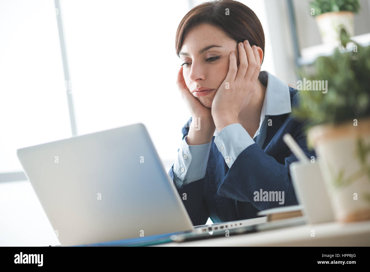 Depressed bored businesswoman working at office desk and networking with a laptop, boring job concept Stock Photo