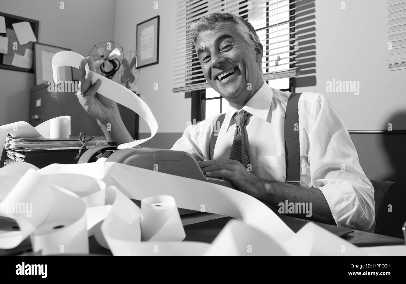 Cheerful vintage accountant smiling and working with adding machine in vintage 1950s office. Stock Photo