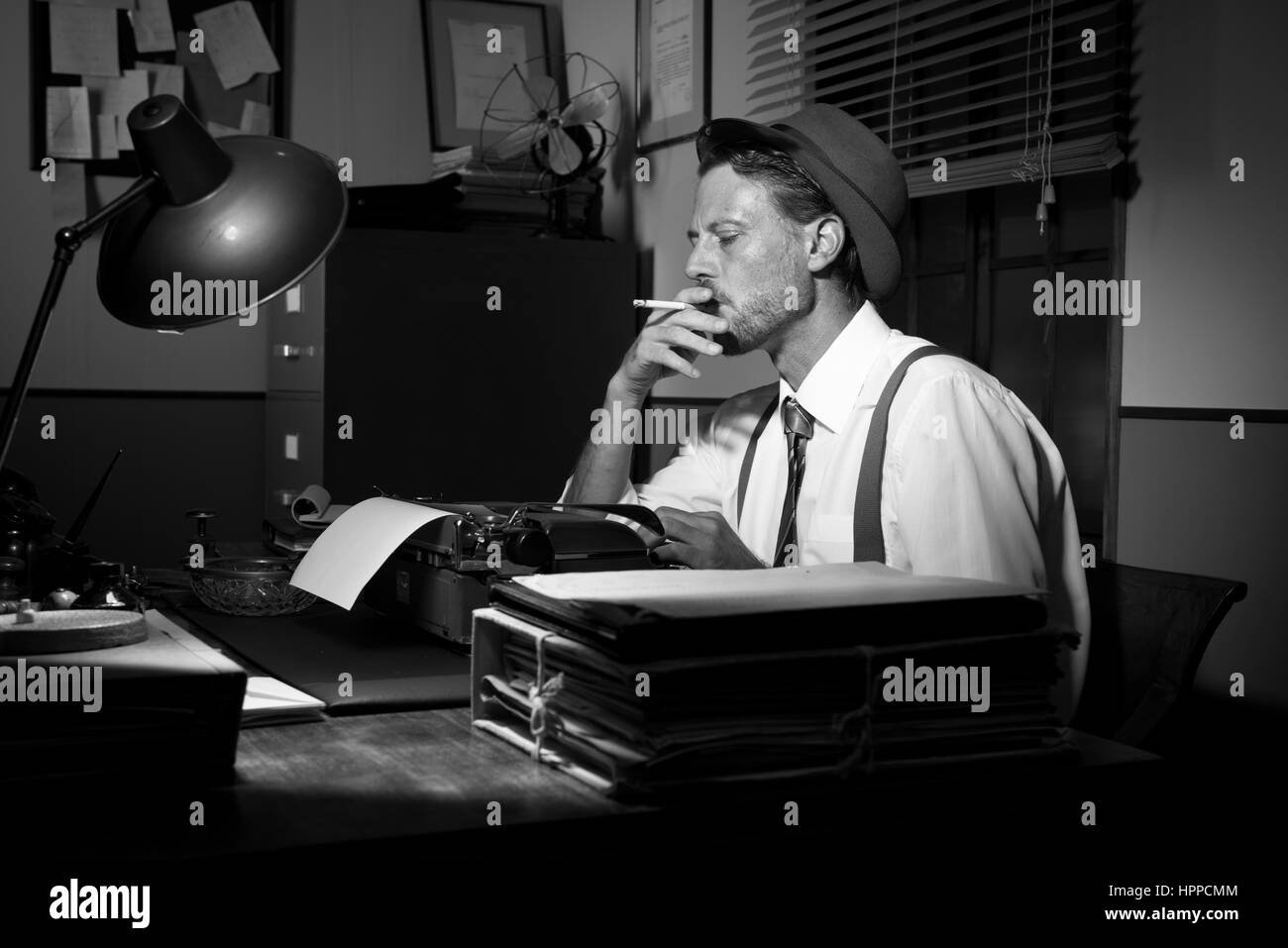 Retro reporter working late typing on a typewriter and smoking a ...