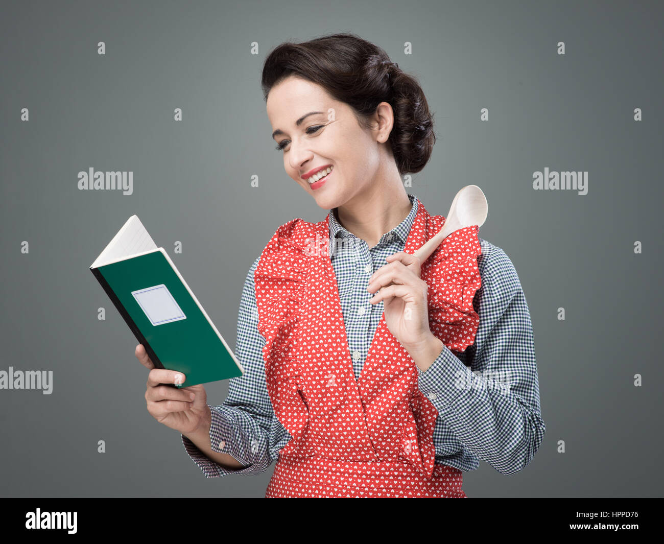 Smiling vintage woman holding an open cookbook and a wooden spoon Stock Photo