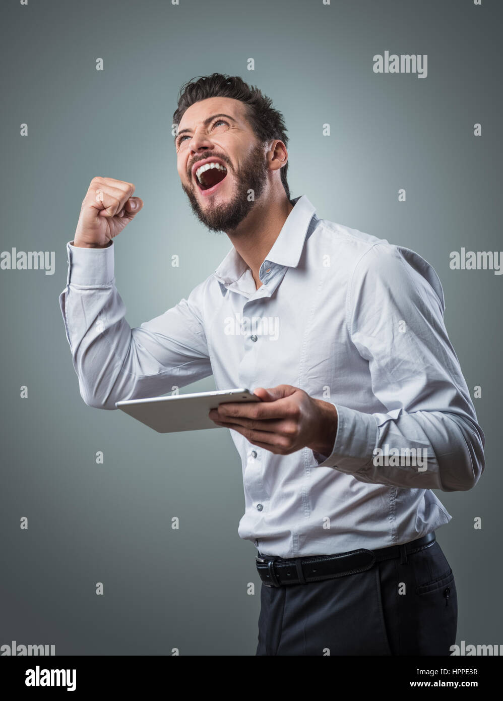 Cheerful smiling man receiving good news on tablet with fist raised ...