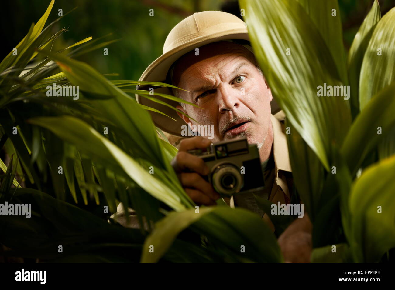 Explorer hiding in vegetation and taking pictures with vintage camera. Stock Photo