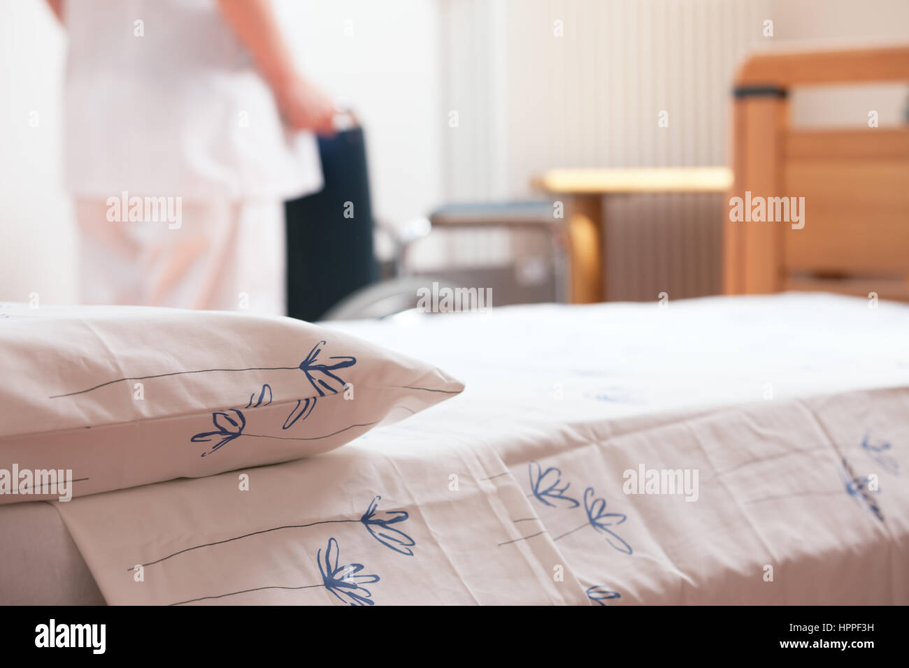 Bed at nursing home with nurse and wheelchair on background. Stock Photo