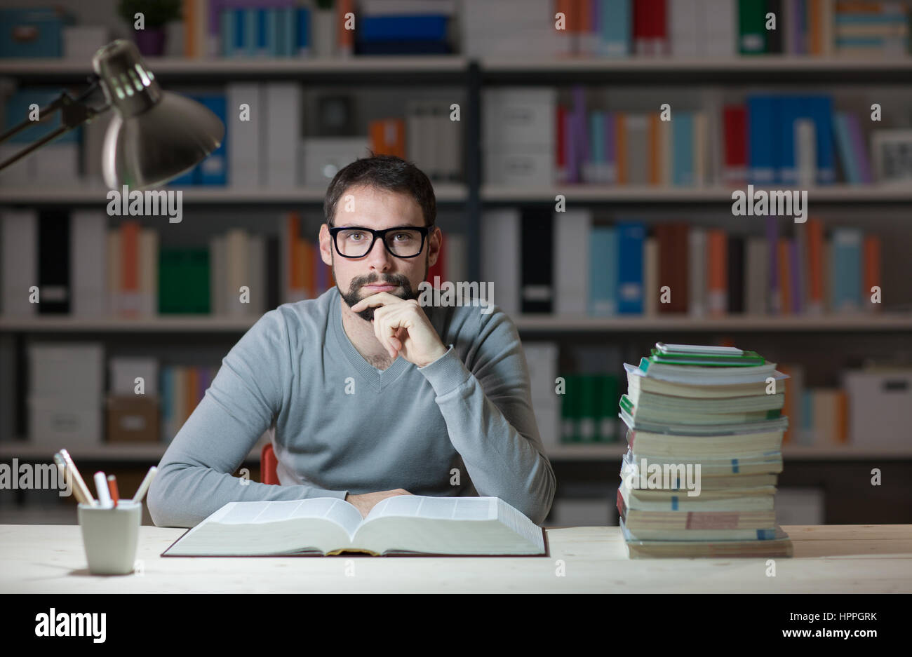 Confident adult student at the library late at night, he is sitting at ...