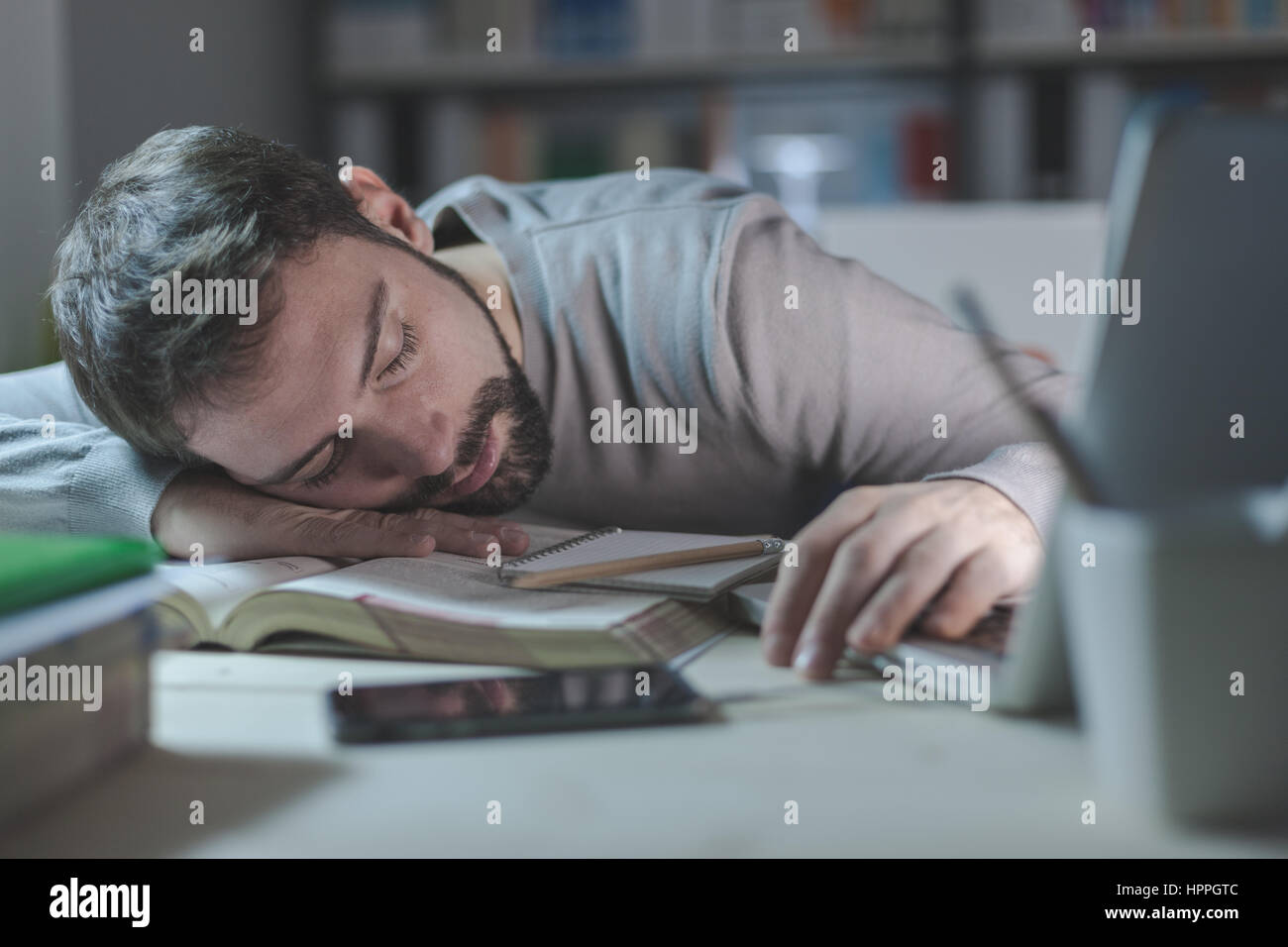 Young exhausted man in the office late at night sleeping on his desk on