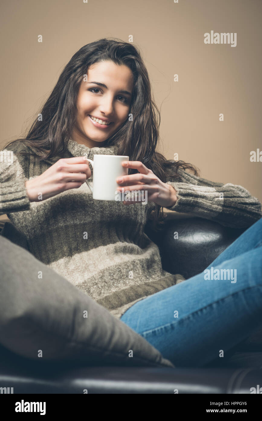 Smiling woman drinking an hot drink sitting on a sofa Stock Photo - Alamy
