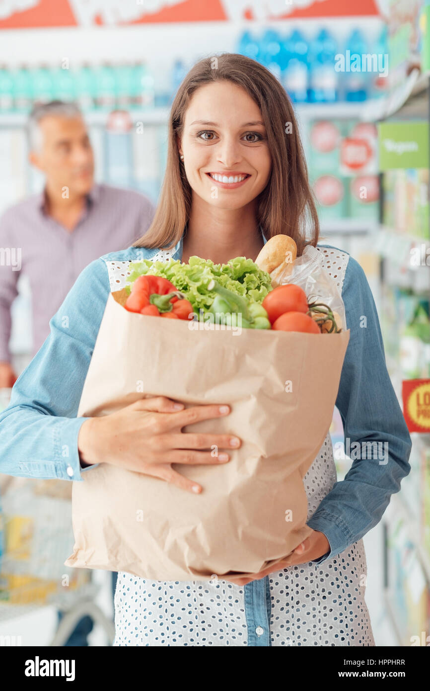 Smiling young woman doing grocery shopping at the supermarket, she is
