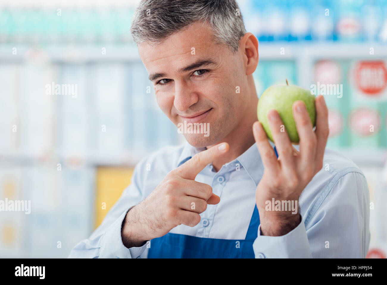 Smiling supermarket clerk showing a fresh apple, freshness and top quality food concept Stock Photo