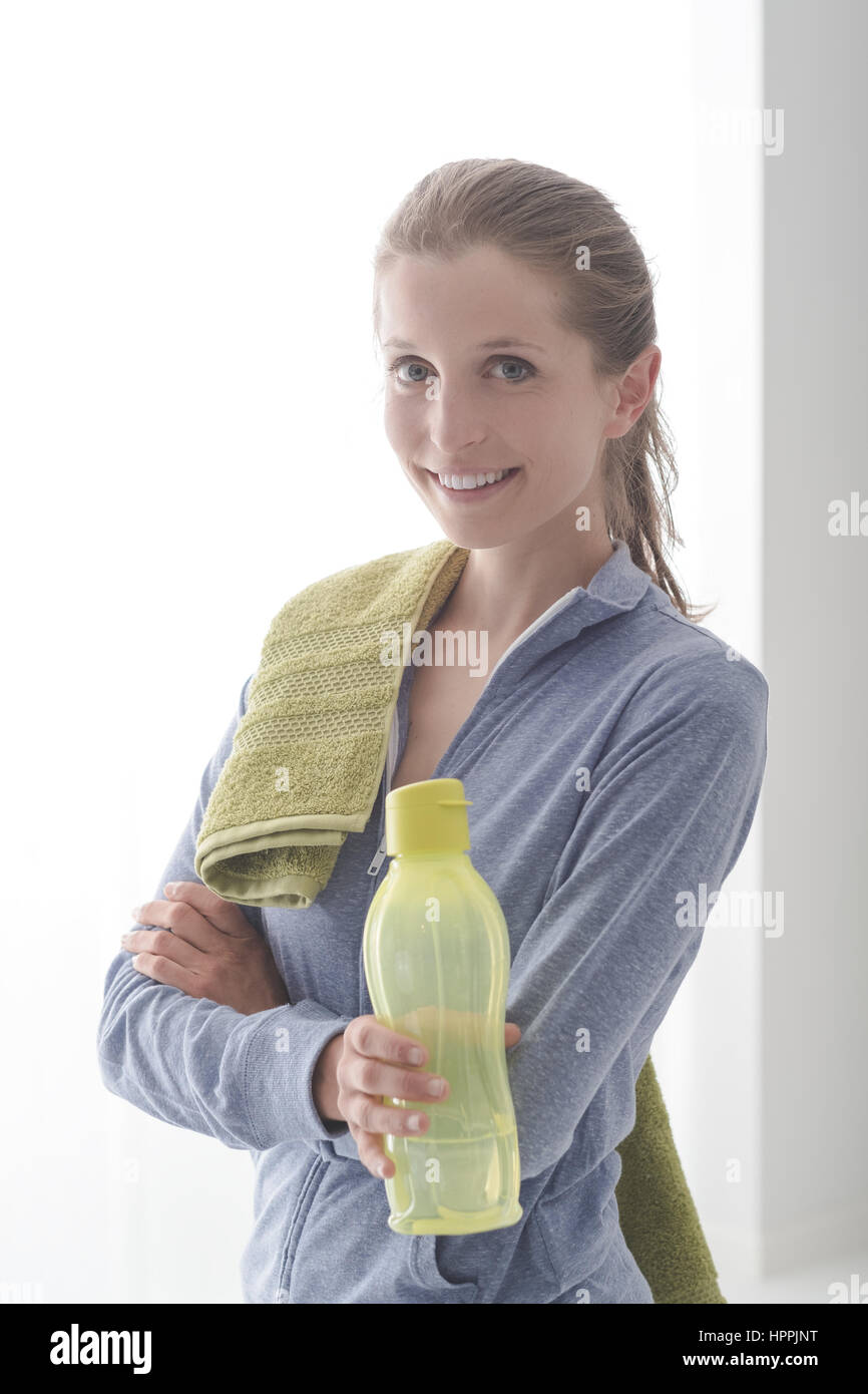 Smiling confident woman posing with a towel and a water bottle after ...