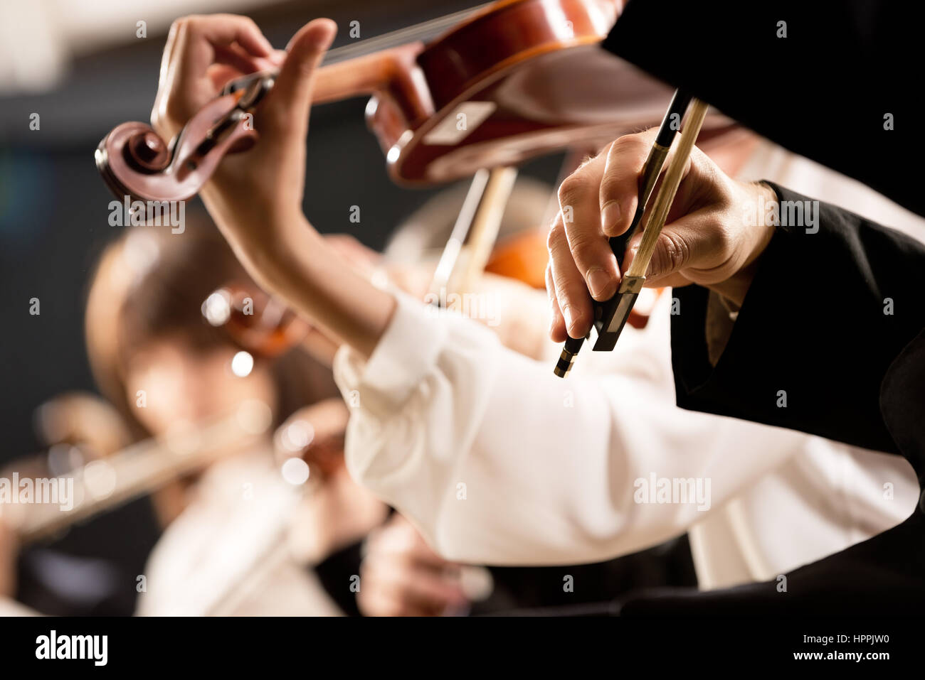 Elegant violin players, hands close-up and orchestra on background. Stock Photo