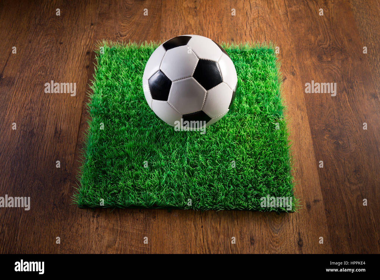 Soccer ball and artificial grass patch on hardwood floor. Stock Photo