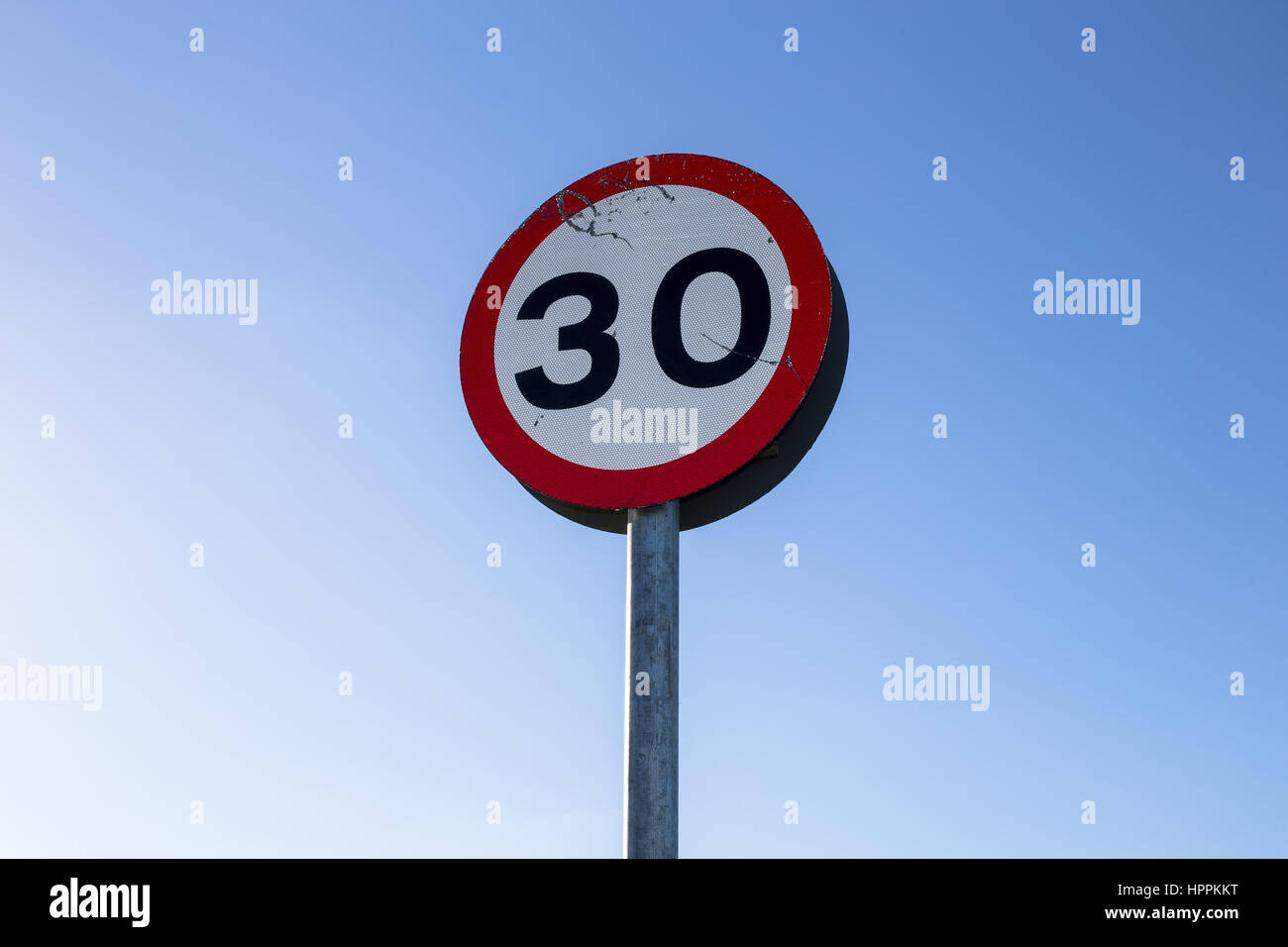 A speed limit sign stands against a blue sky indicating a maximum permissible speed of 30 mph in the village of Bishops Lydeard, Somerset, UK. Stock Photo