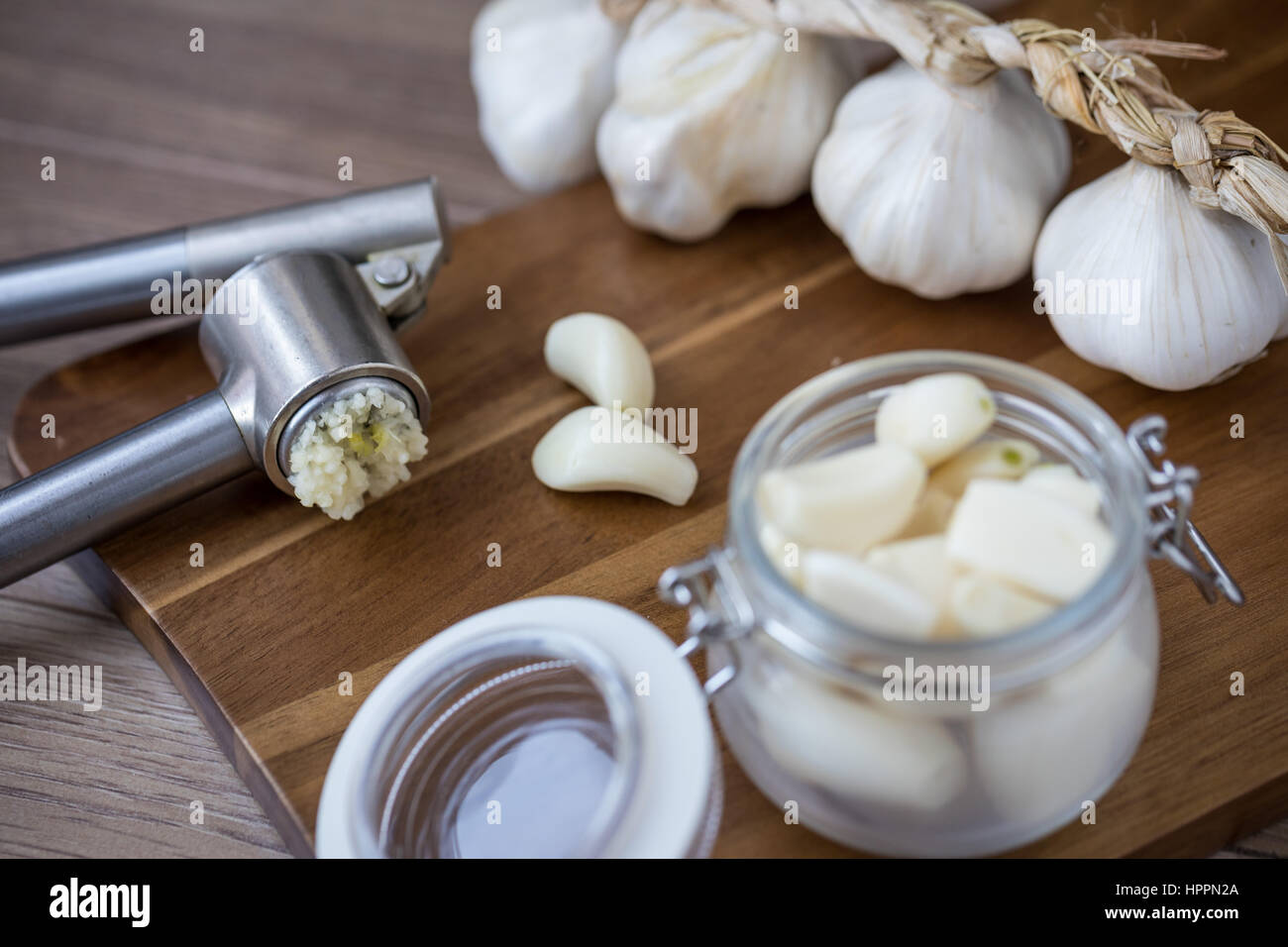 Peeled garlic in a glass container with garlic clove and bulb and a garlic press Stock Photo