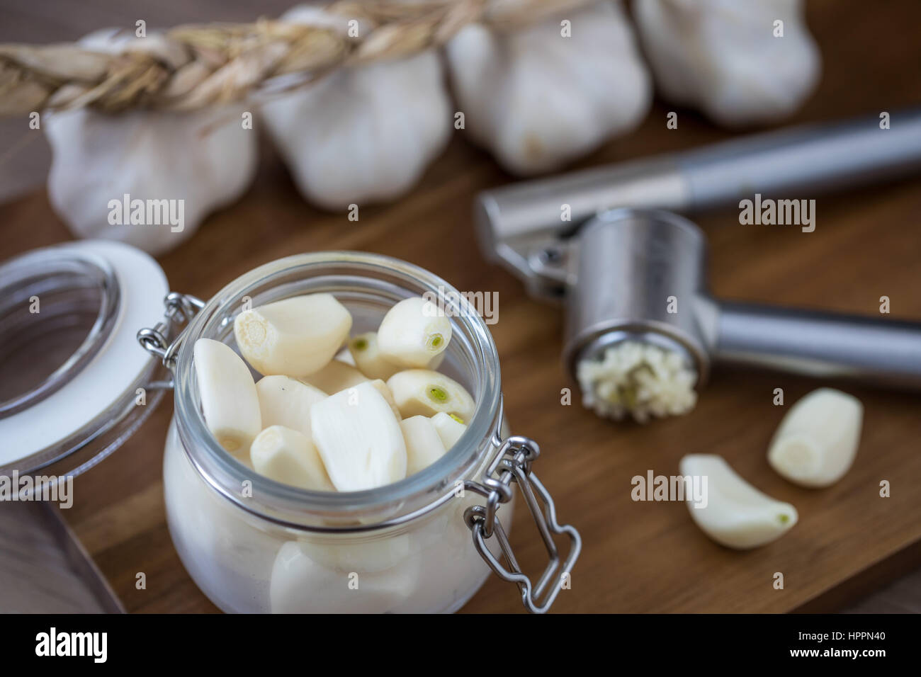 Peeled garlic in a glass container with garlic clove and bulb and a garlic press Stock Photo
