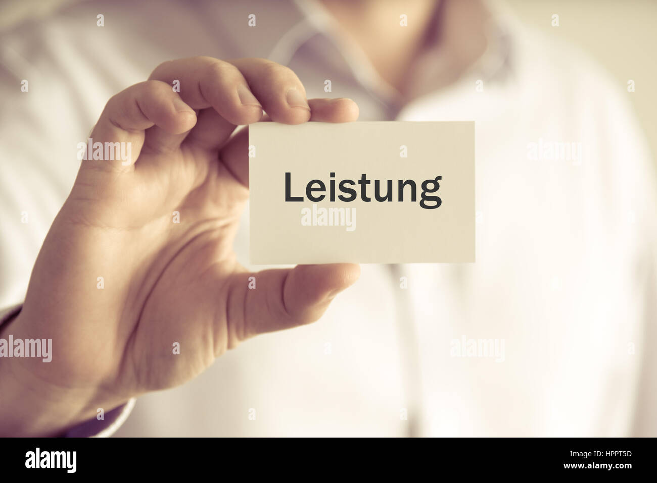 Closeup on businessman holding message card 'LEISTUNG' written in German - translation : Power, business concept image with soft focus background and  Stock Photo