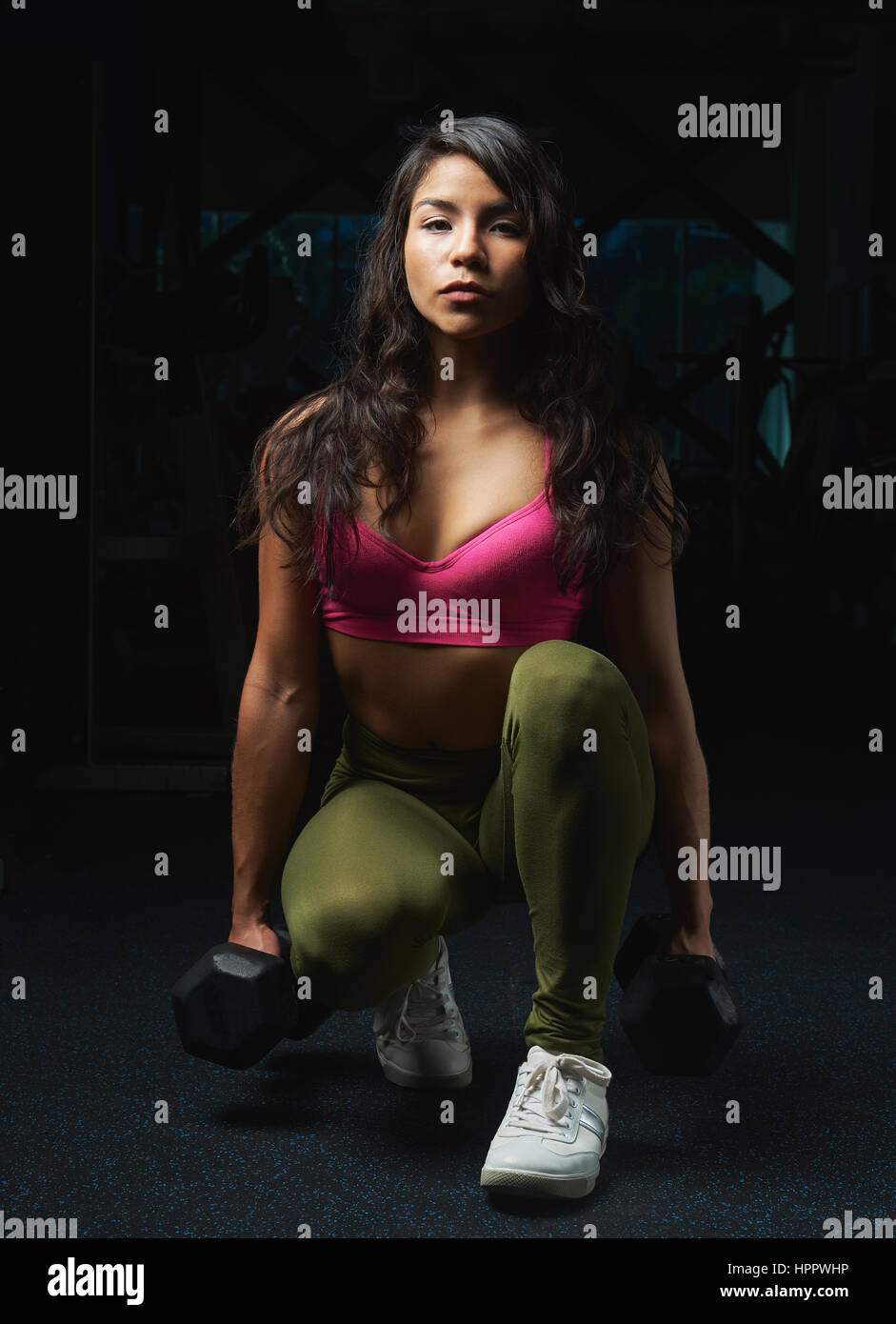 Sporty woman sitting with dumbbells on modern gym background. Training exercise with weights doing young skinny girl Stock Photo