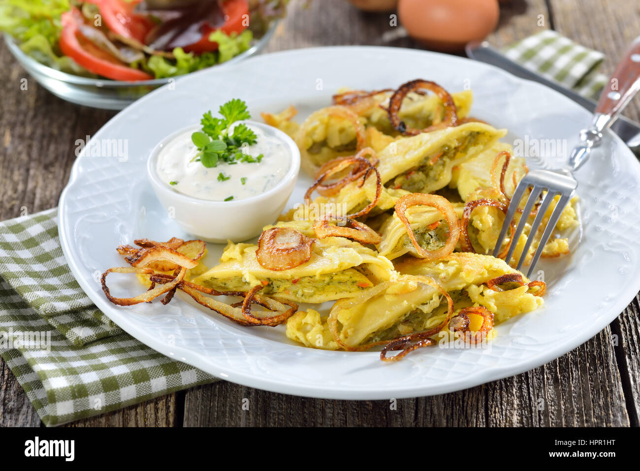 Fried Swabian ravioli (so-called'Maultaschen') with vegetarian filling served with roasted onions, scrambled egg and creamy herb cheese Stock Photo