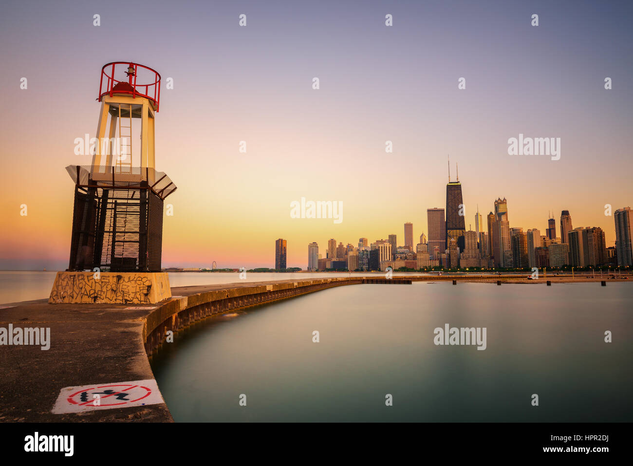 Chicago skyline across Lake Michigan at sunset viewed from North Avenue Beach with a lighthouse in foreground. Long exposure. Stock Photo