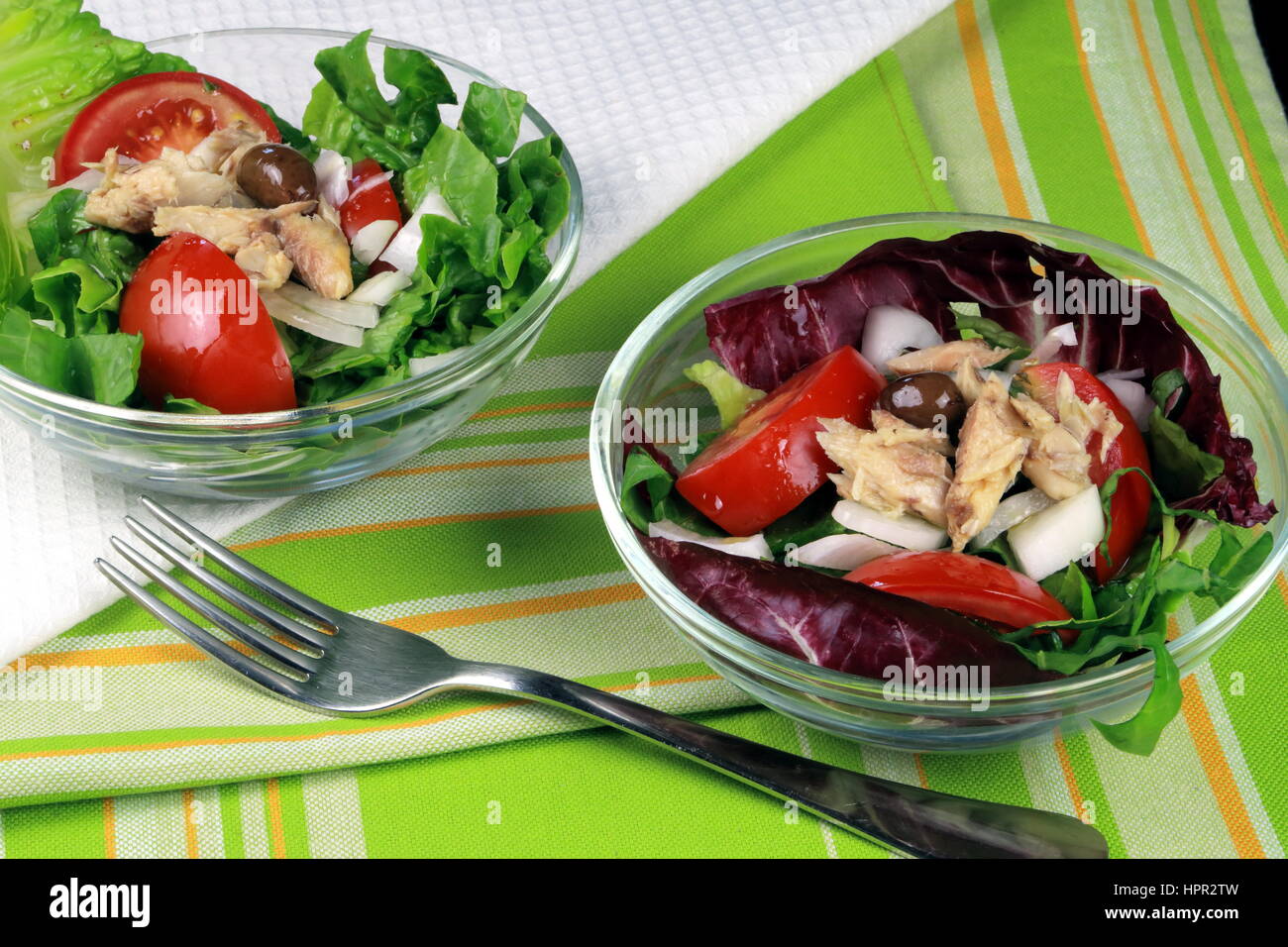 Lettuce, tomato, olive and mackerel summer salad served in glass bowls on colorful kitchen cloth with fork - Healthy food for green living Stock Photo