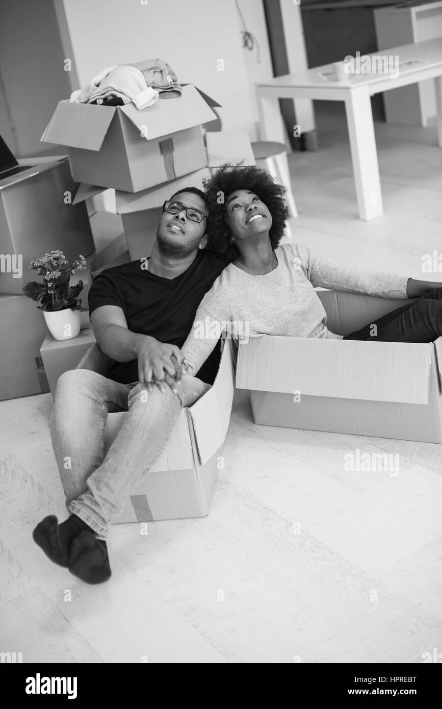 African American couple sitting in a box playing with packing material, having fun after moving in new home Stock Photo