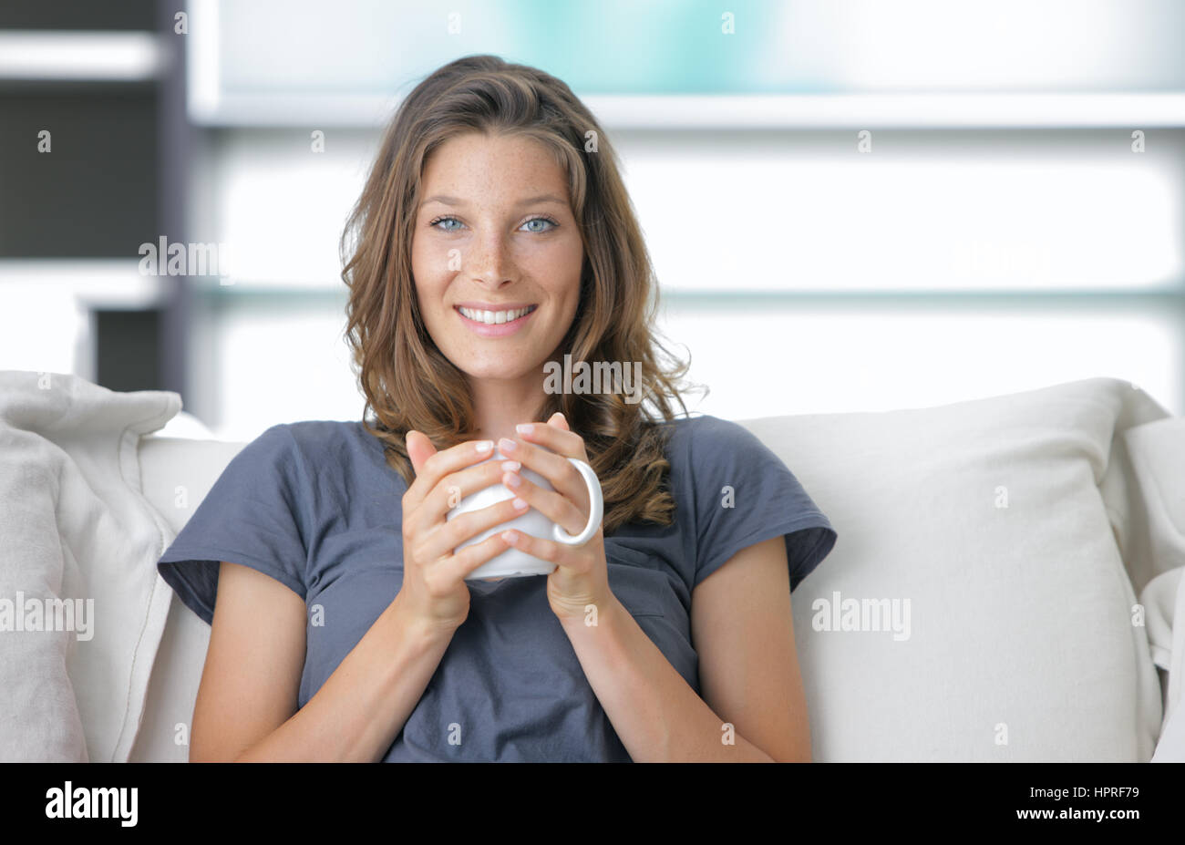 Portrait of a cute young lady sitting on sofa with a cup of coffee ...