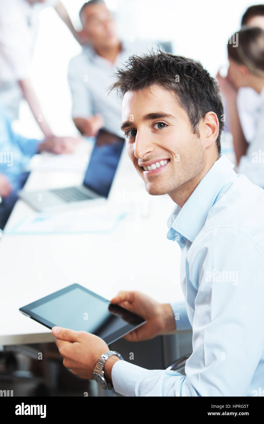 Portrait of a young businessman using his digital tablet, colleagues in ...