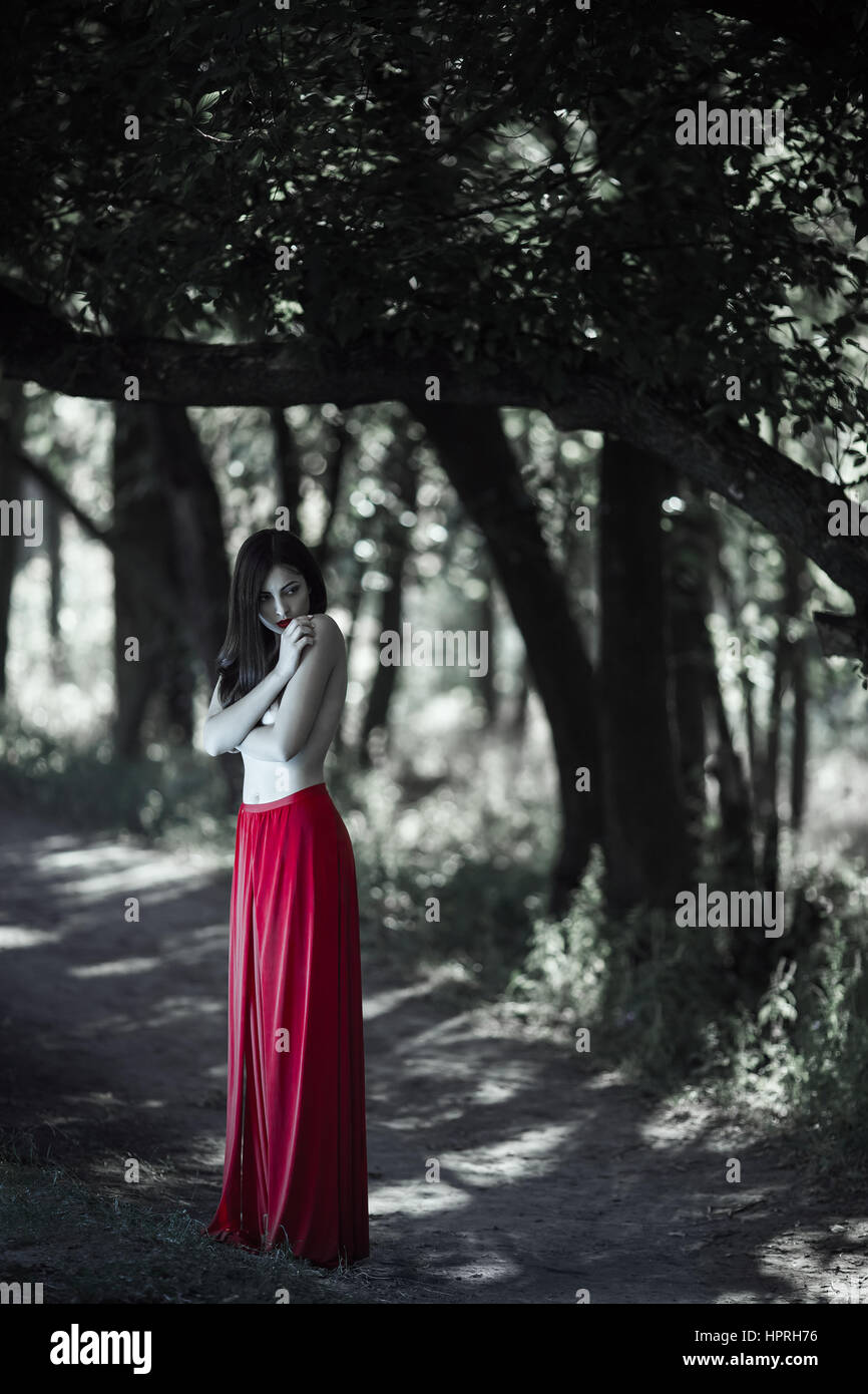 Wonderful sexy fashion model with naked walking in a fantastical forest.  Photo of seductive nude woman in full length in luxury long red dress  posing Stock Photo - Alamy