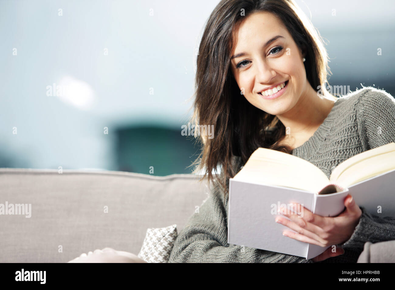 Portrait of a happy young woman lying on couch with book Stock Photo ...