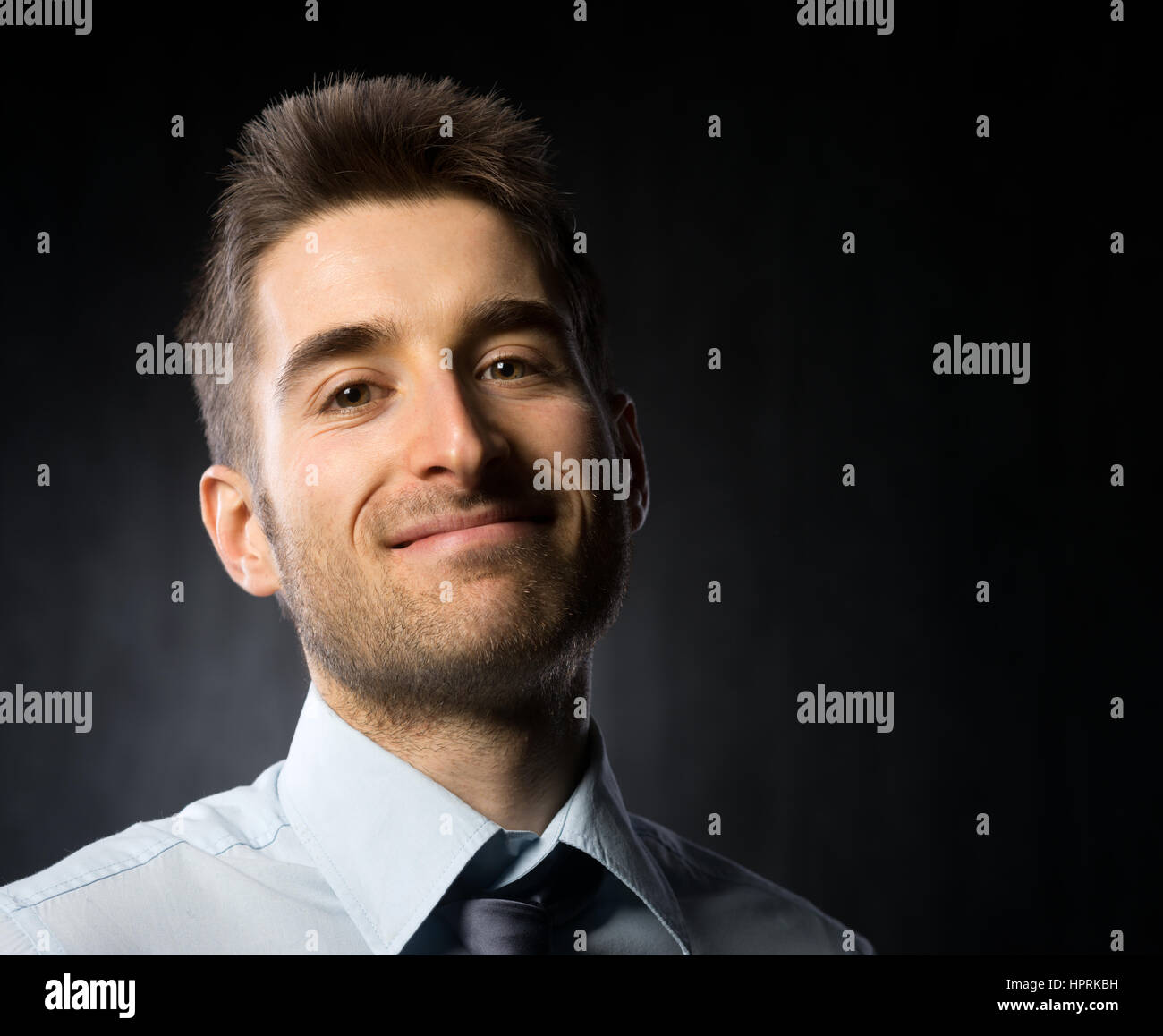 Attractive young businessman looking at camera and smiling on dark ...