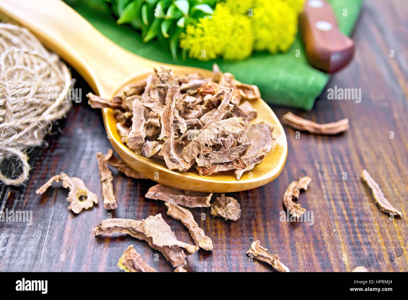 Spoon the dry root of Rhodiola rosea, knife, fresh flowers, a skein of twine on a wooden boards background Stock Photo