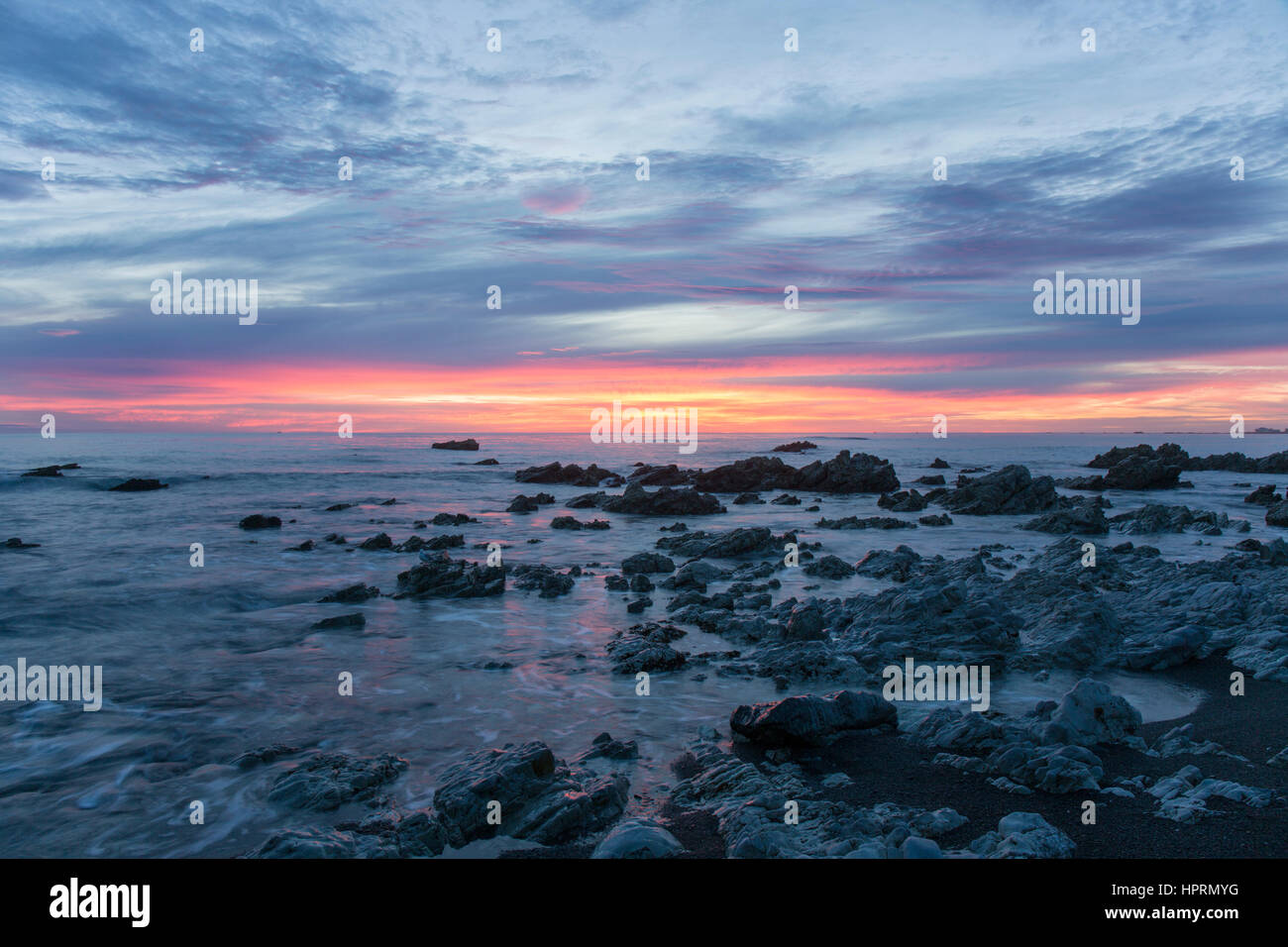 Kaikoura, Canterbury, New Zealand. View across the Pacific Ocean from rocky shoreline at dawn, pink sky reflected in water. Stock Photo