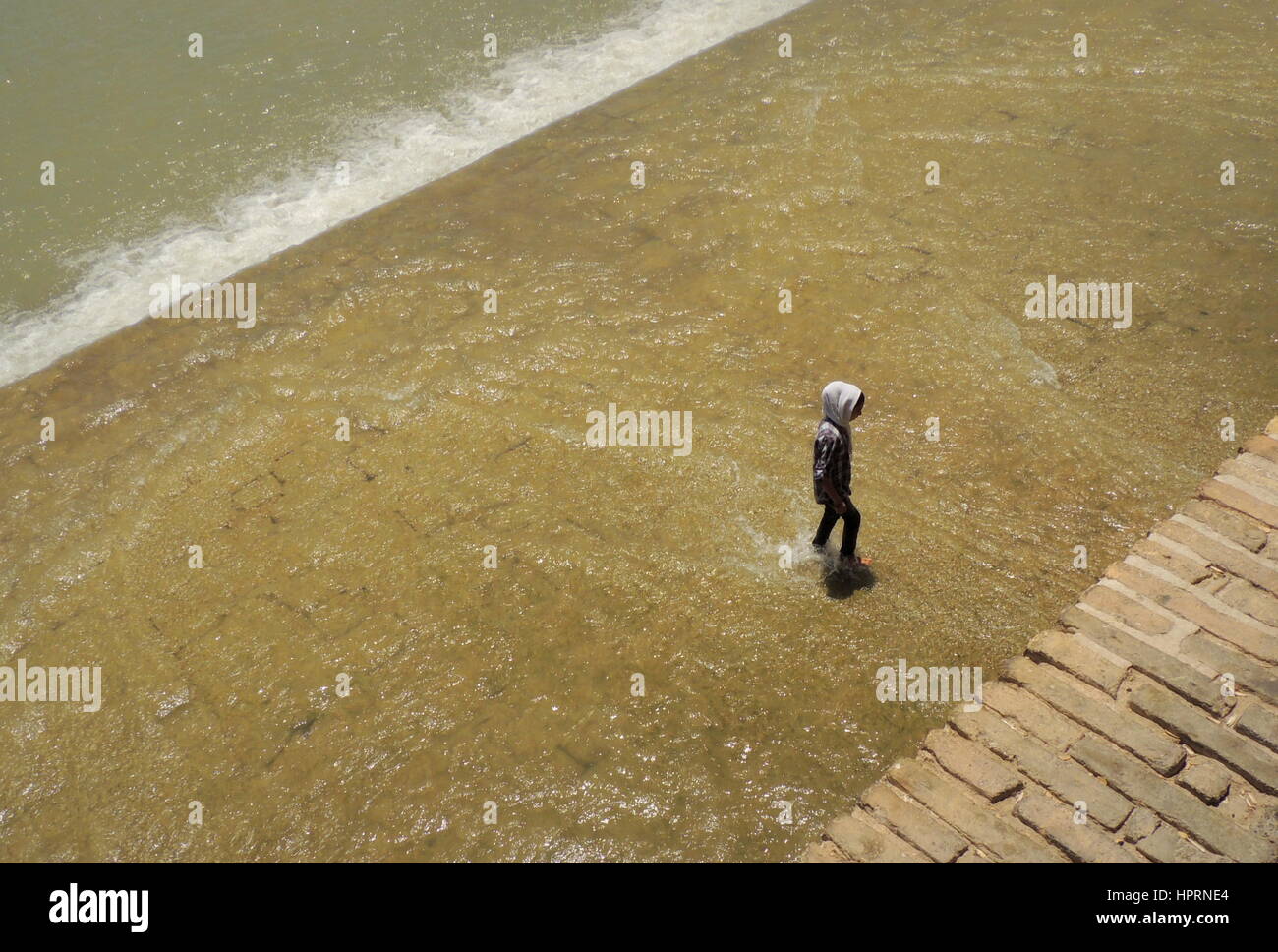 Muslim girl goes against the flow and walks alone challenging the waters of the Zayandeh river by the Si o seh pol bridge - Isfahan, Iran Stock Photo