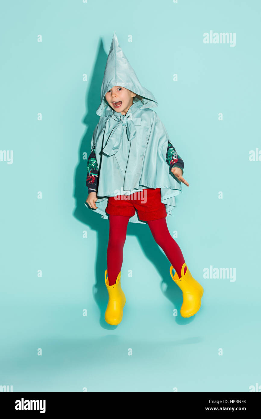 Little girl posing in fashion style wearing autumn clothing on blue background. Rubber yellow