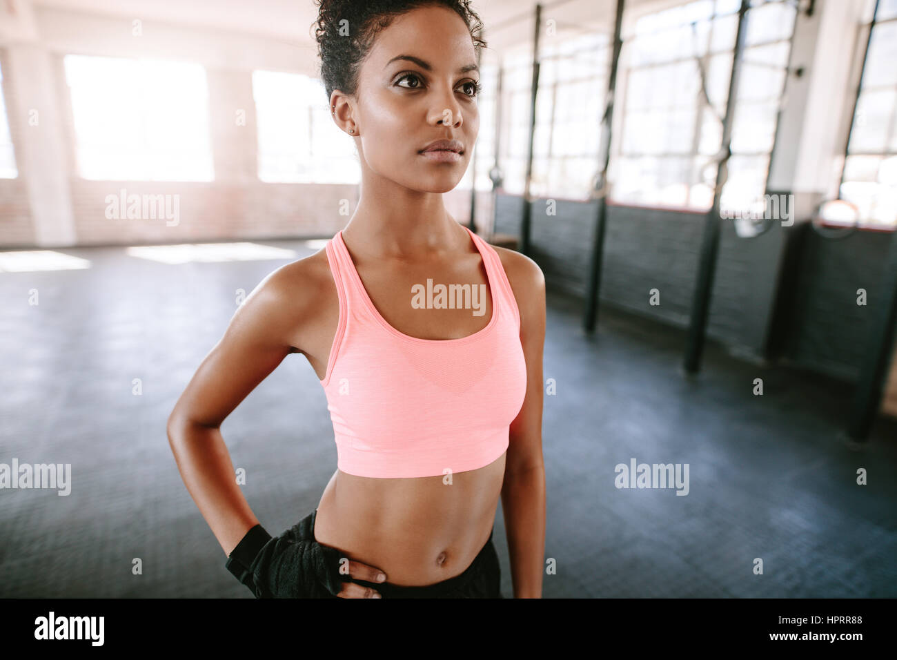 Portrait of healthy young female model standing in gym. Fitness woman in sportswear looking away. Stock Photo