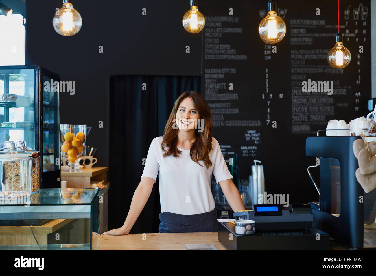 Young female barista standing behind the bar in cafe smiling Stock Photo