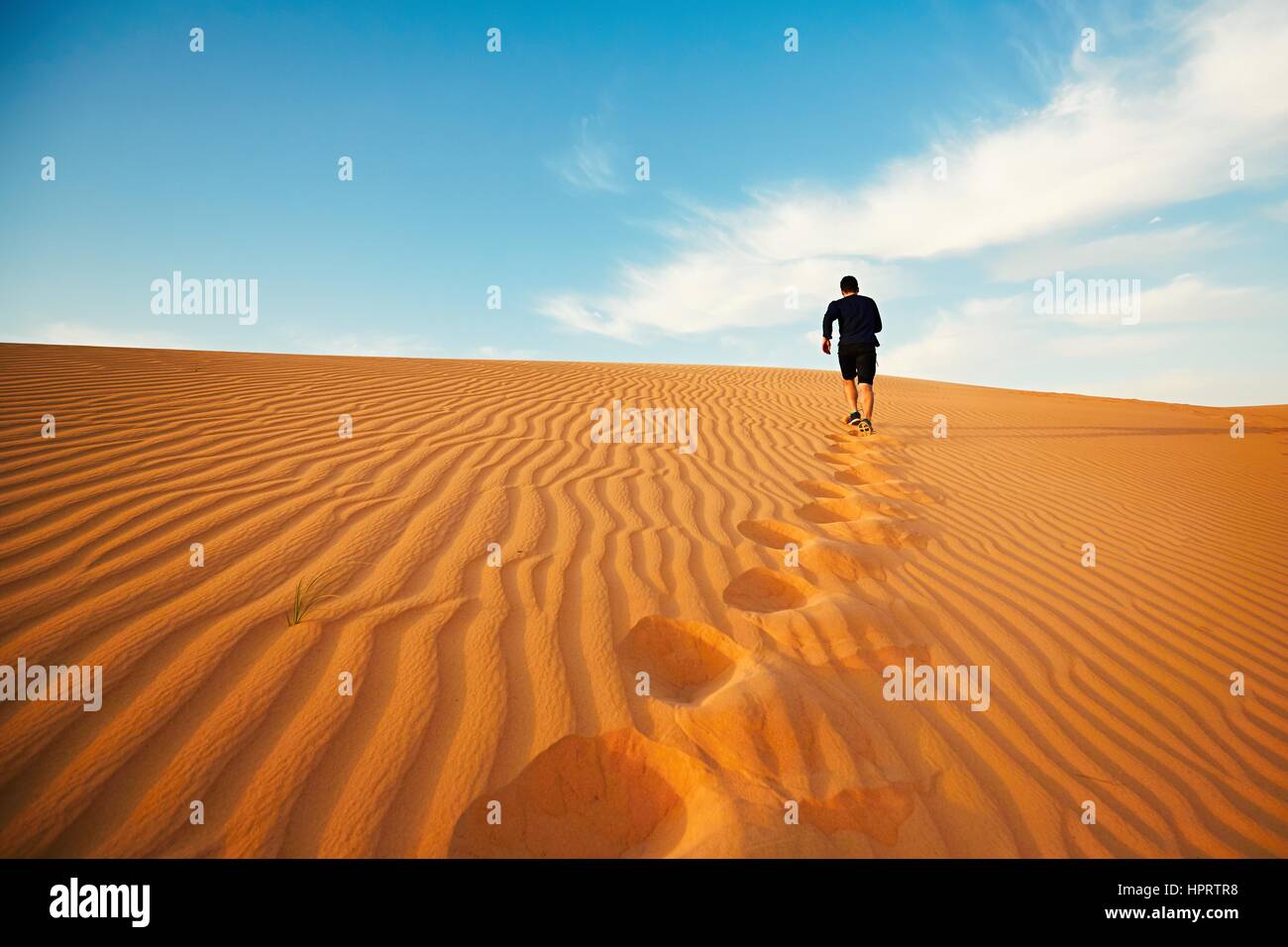 Young man is running to the top of dune in desert Stock Photo - Alamy
