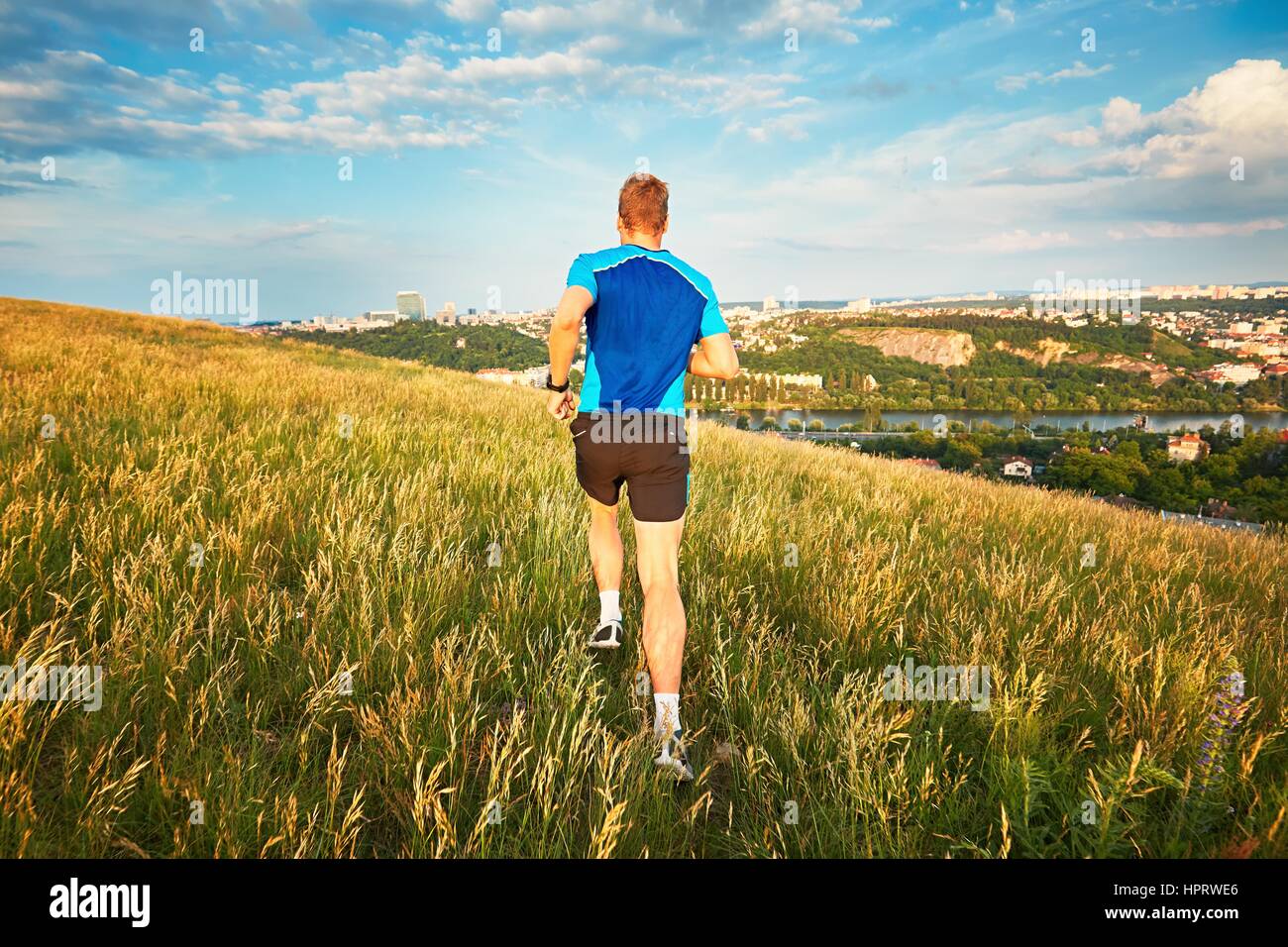 Sport lifestyle. Athletic young man is running on the hillside outside the city. Prague, Czech Republic. Stock Photo