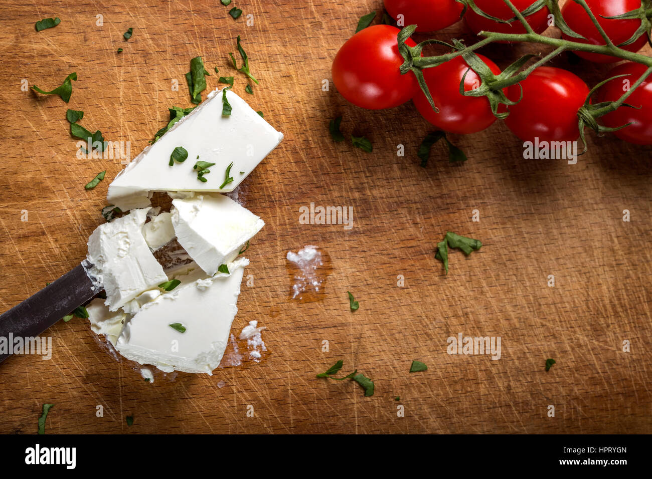 Feta cheese with knife and bunch of cherry tomatoes on wood with herbs Stock Photo
