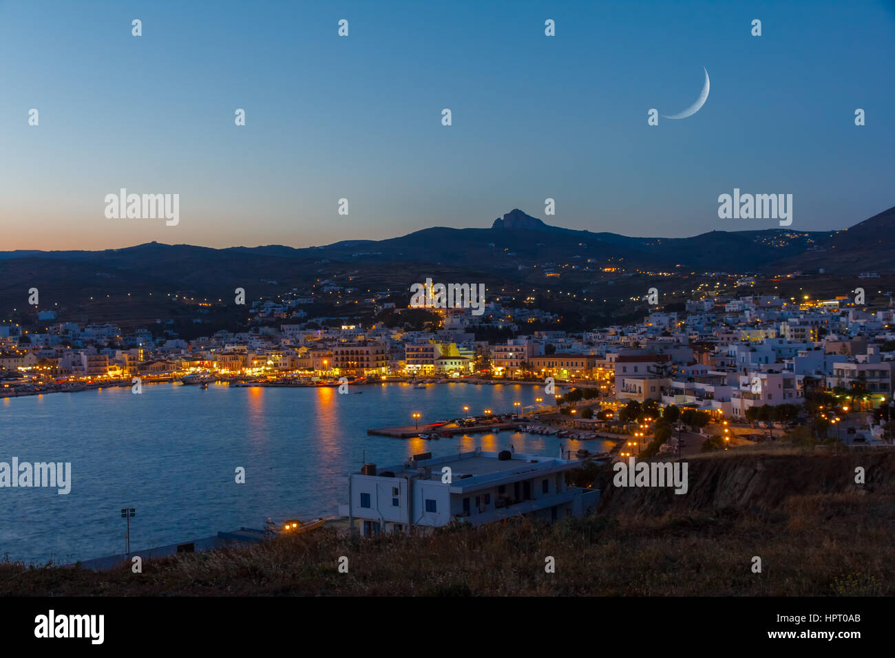 Tinos city and harbor in the afternoon with the moon rising above the sky Stock Photo